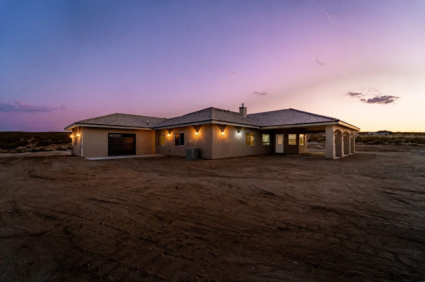 Rear twilight view of a completed custom desert home with a covered patio and exterior lighting