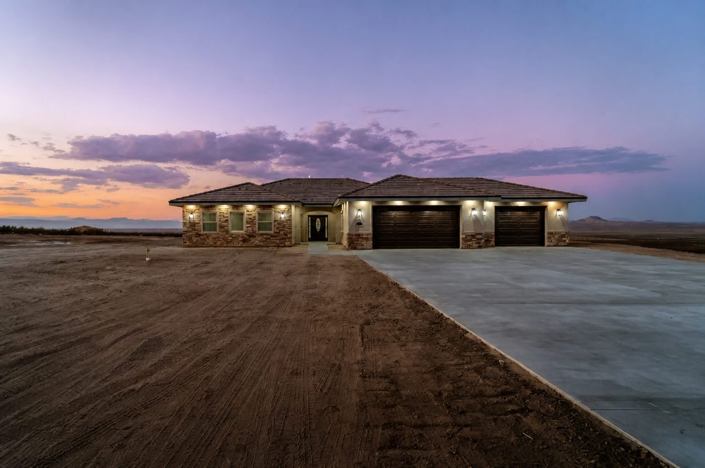 Completed custom home at twilight with lit windows and a wide concrete driveway