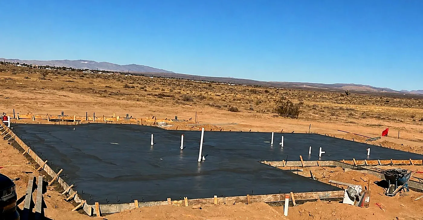 Poured concrete foundation slab on open desert acreage, plumbing stubs standing, mountains on the horizon
