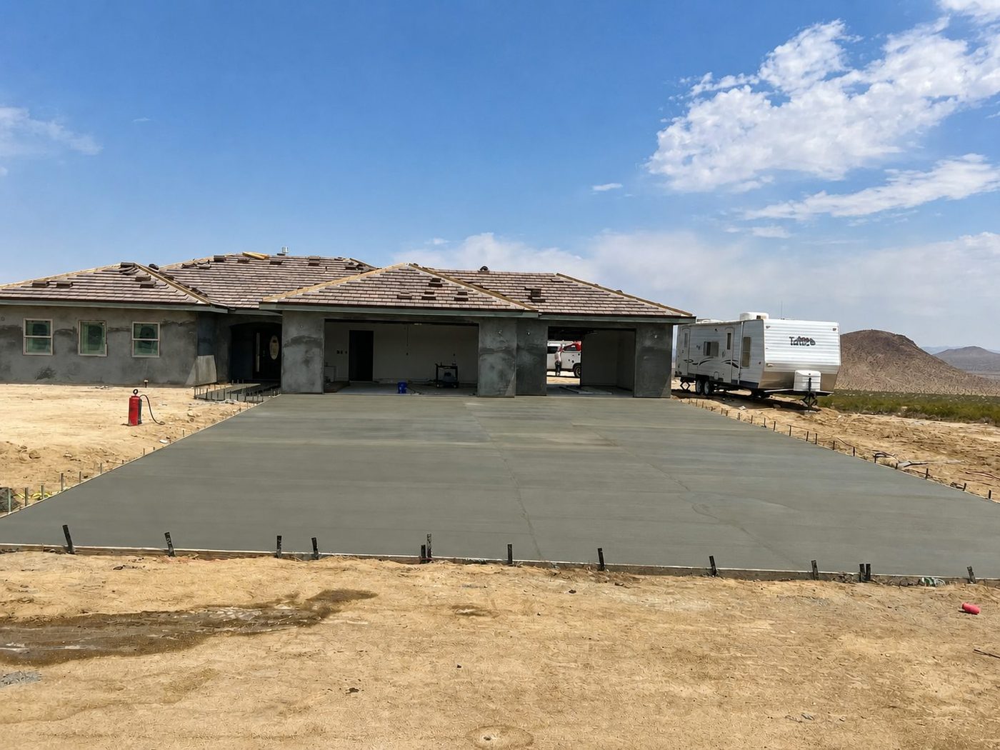 Freshly poured wide concrete driveway in front of a custom home under construction