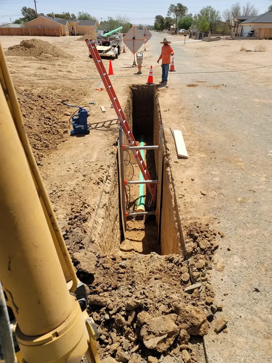 Workers installing a sewer pipe in a deep excavated trench